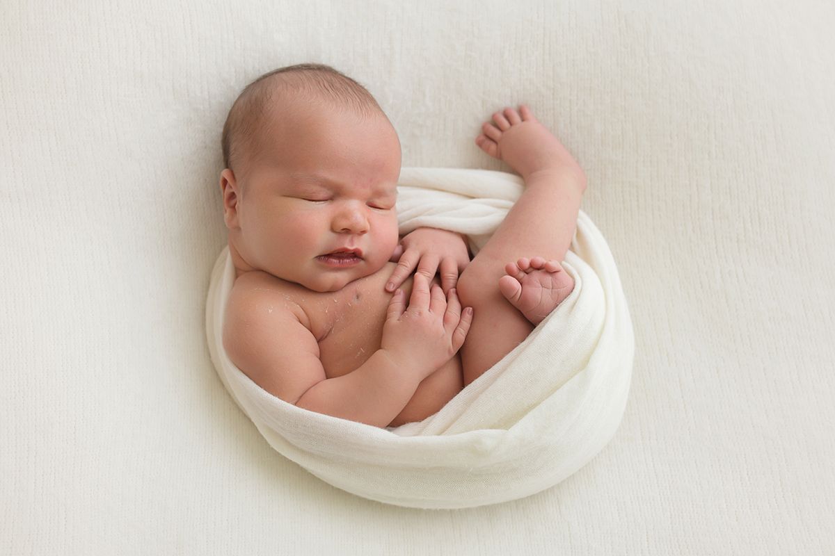 Peaceful newborn baby sleeping on white blanket during studio photography session.