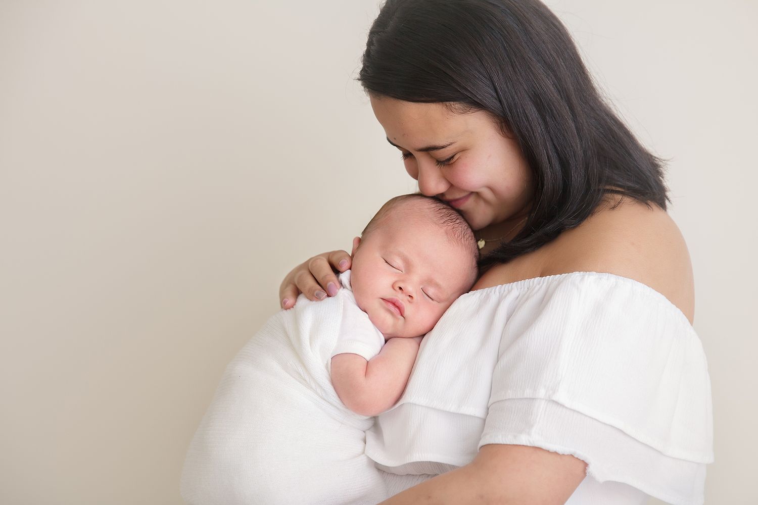 A tender moment between parent and newborn baby wrapped in white against a neutral background.