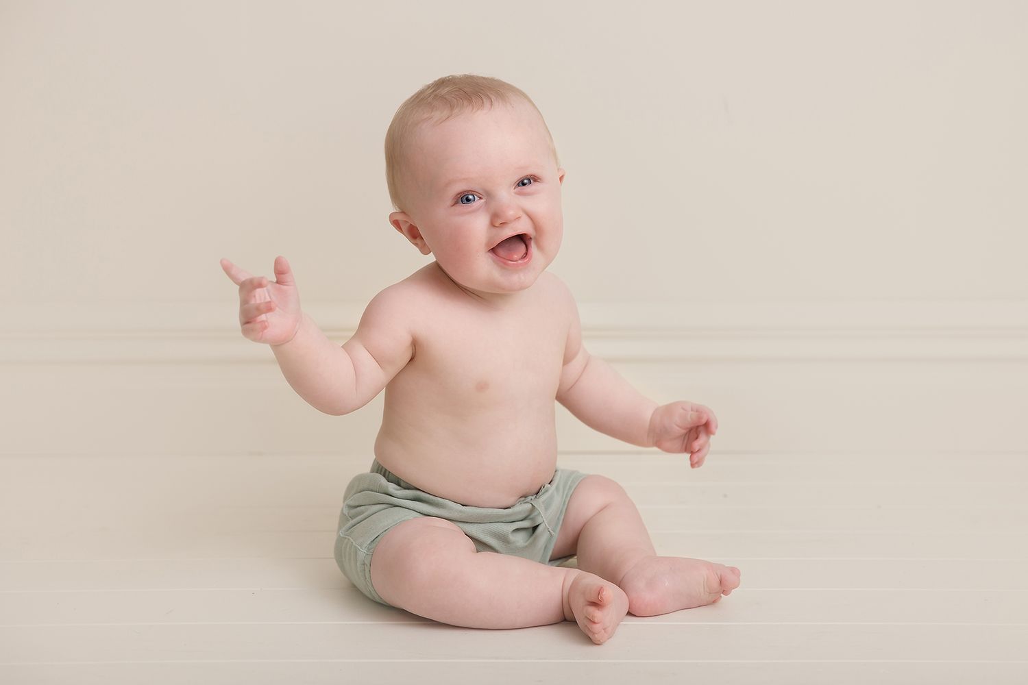 Baby showing joyful expressions during professional photo session on neutral background.