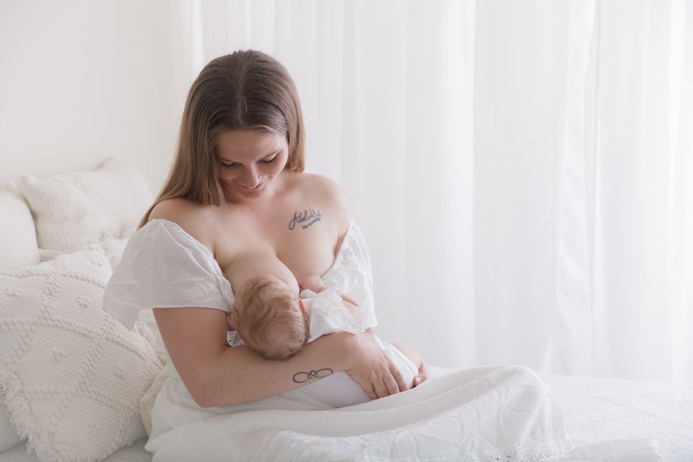 Intimate portrait of mother and newborn baby in soft white bedding.