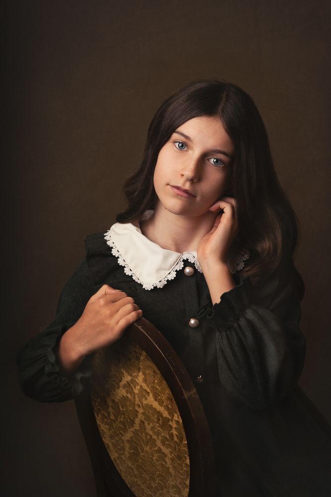Dramatic portrait of young person in vintage dress with lace collar against dark background.