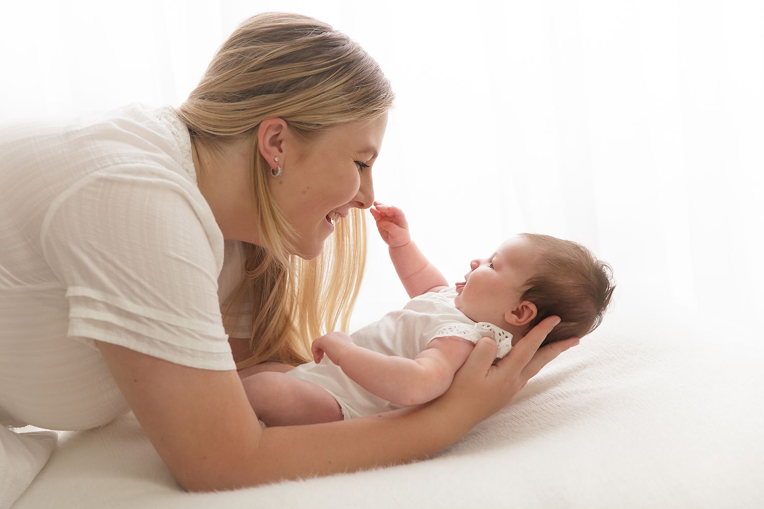 Parent and baby sharing playful moment while lying on white bedding.
