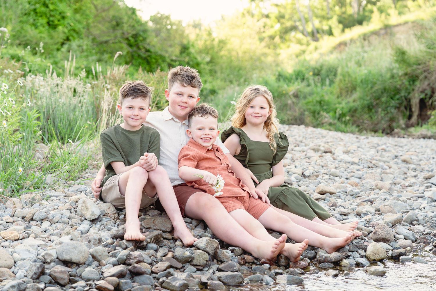 Family group lounges casually on rocky riverbank during golden hour outdoor photo session.