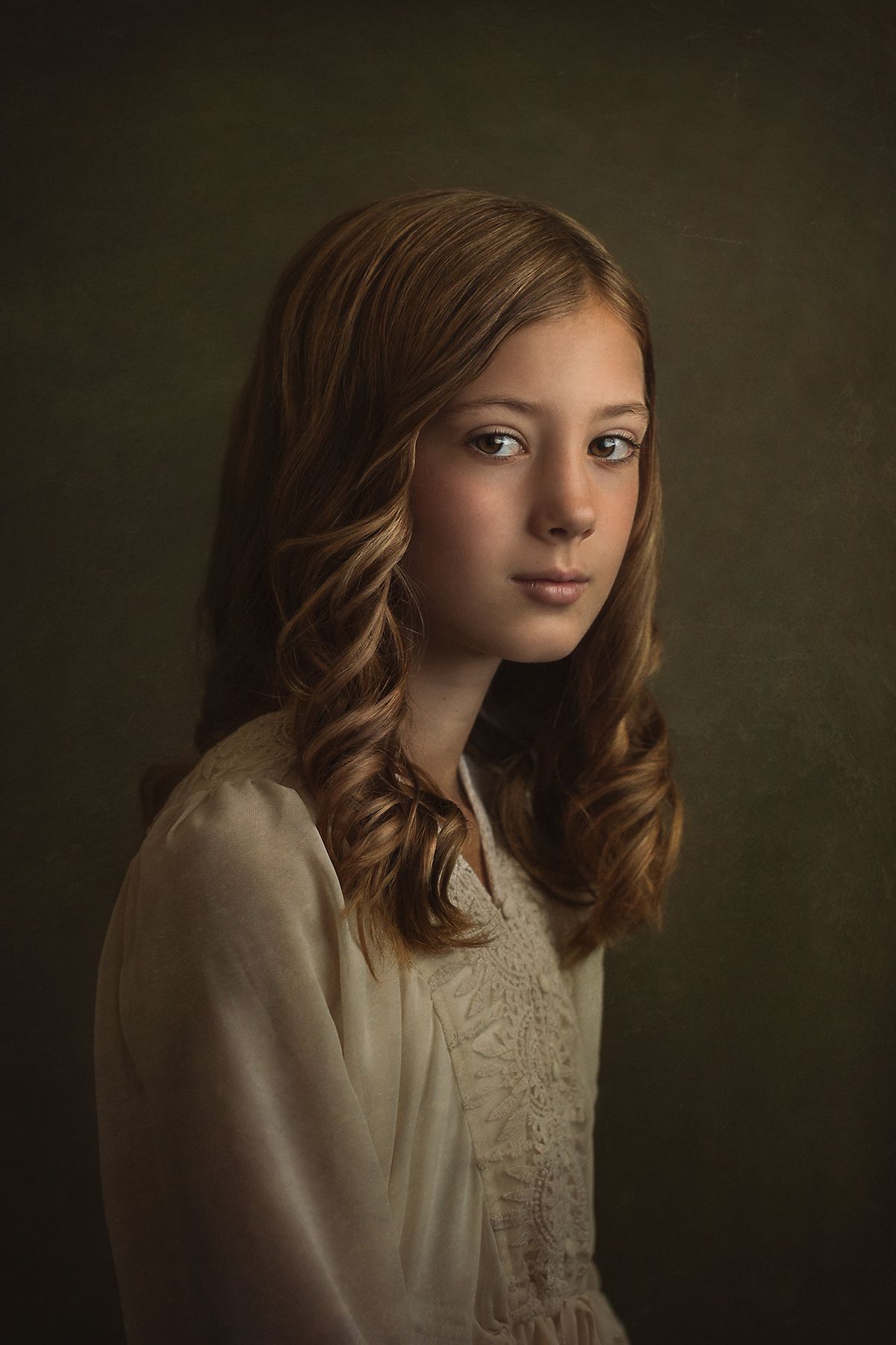 Fine art portrait with soft lighting highlighting an ivory lace blouse against a dark background.