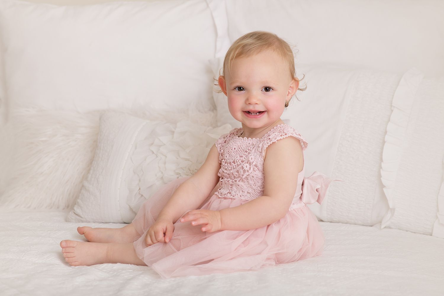 Baby wearing pink dress lies on white couch in series of connected lifestyle portraits.