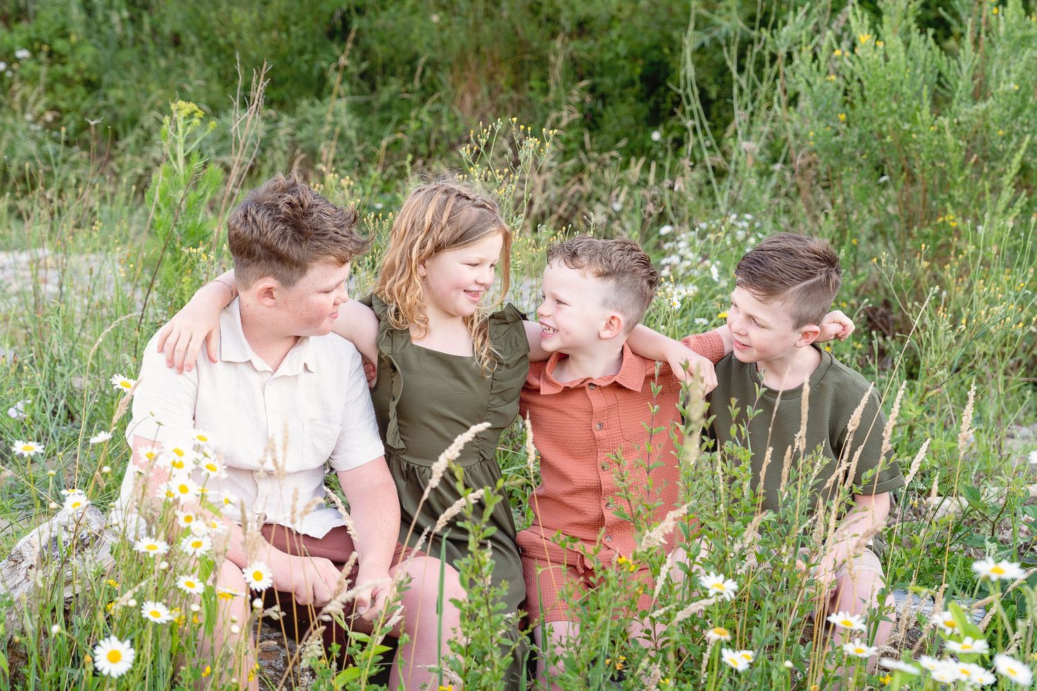 A group of children explore and play together in a lush summer garden filled with wildflowers and tall grasses.