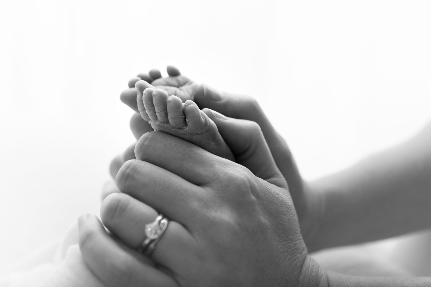 Close-up black and white photo of hands gently cradling a sleeping newborn baby.