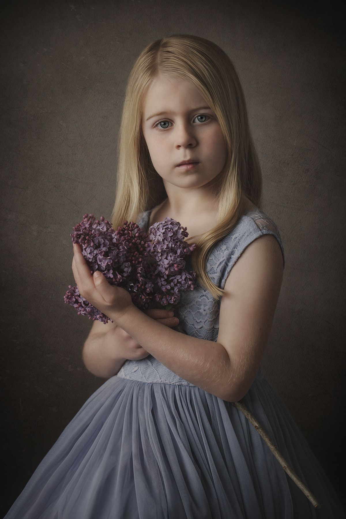 Ethereal portrait in muted tones featuring a blue dress and purple lilac flowers.
