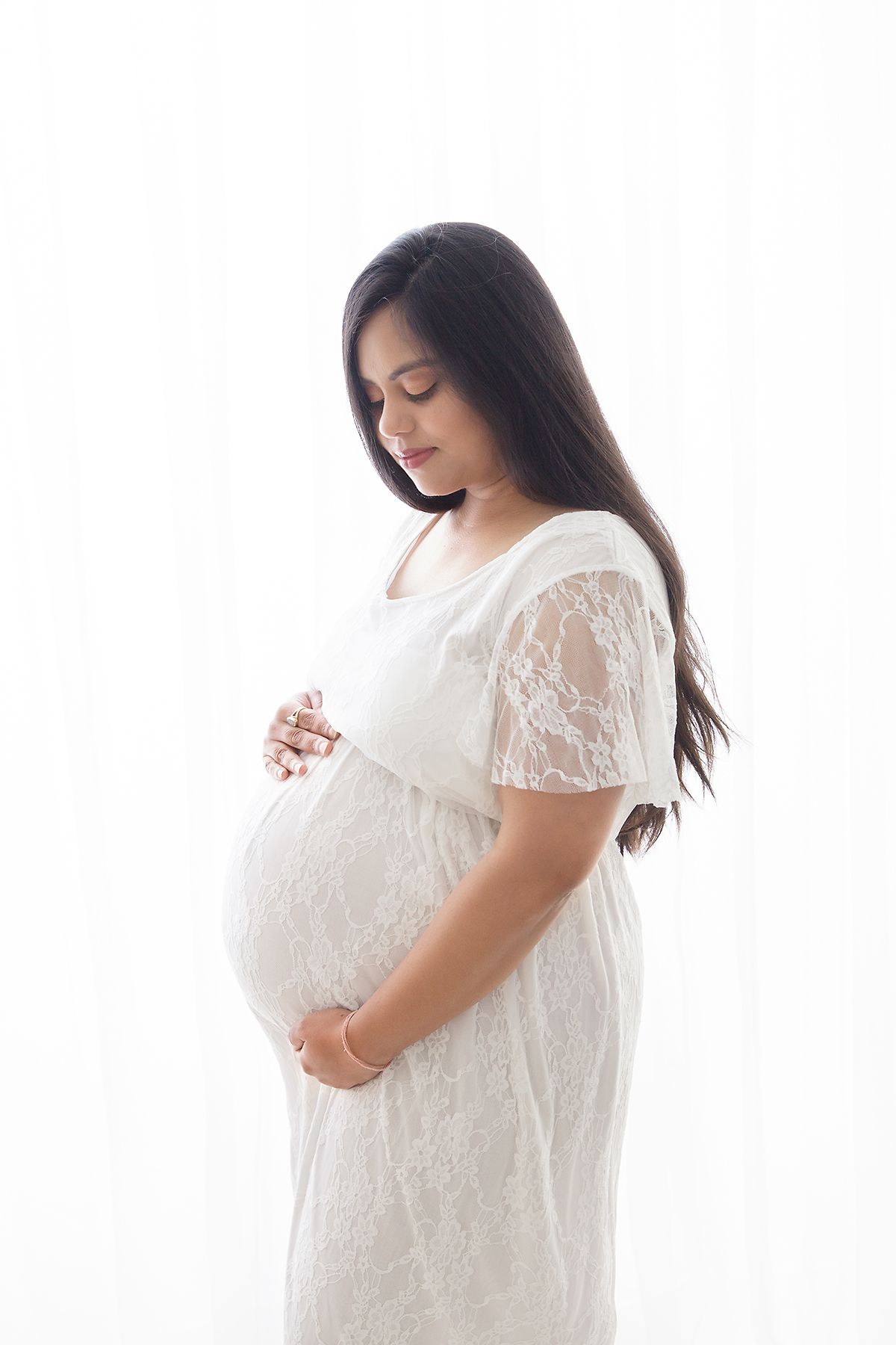 Ethereal maternity photos in white lace dress against bright window light.