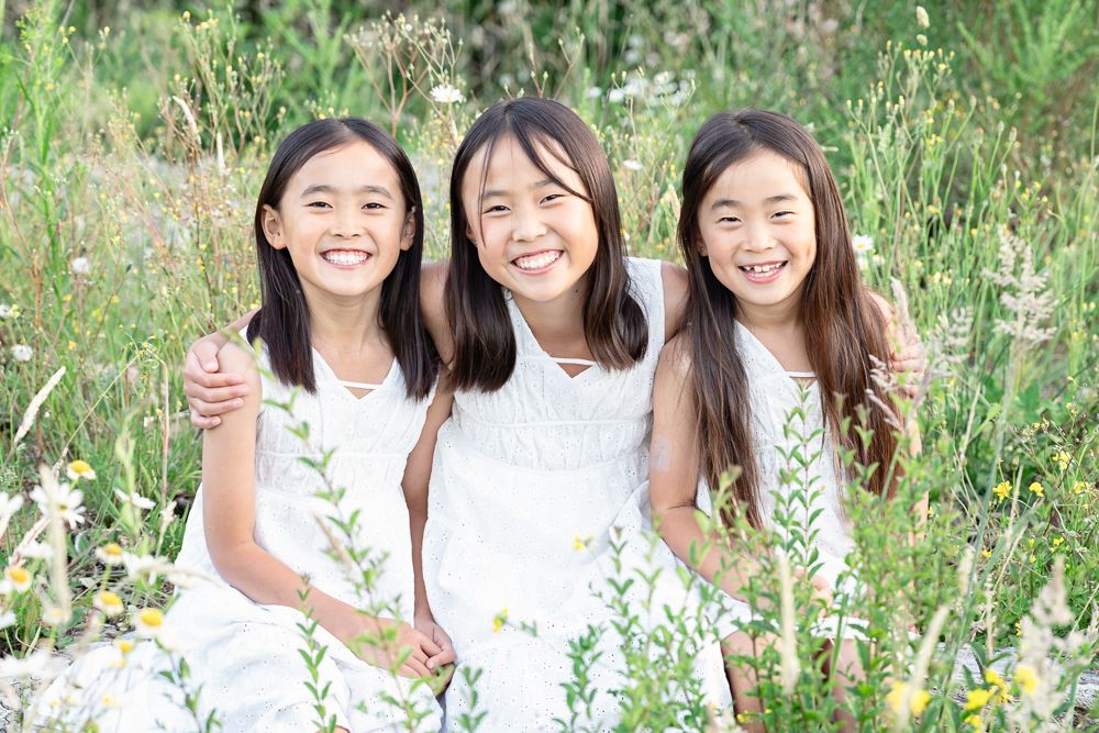 A group in white outfits poses together in a field of wildflowers and tall grass on a sunny day.
