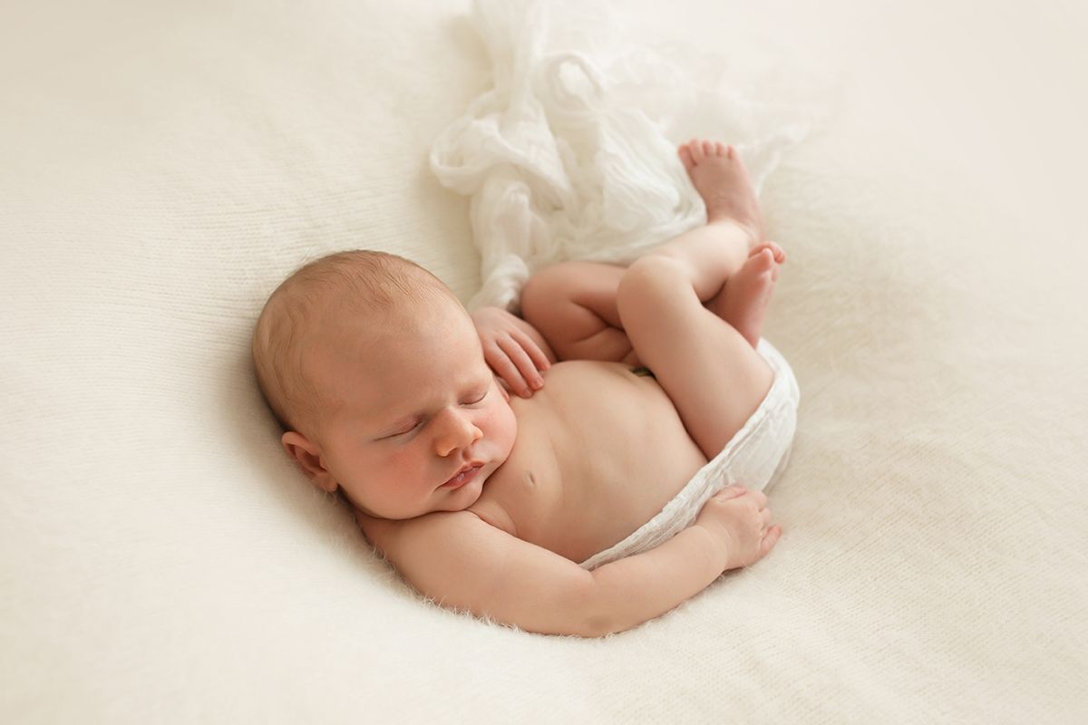 Peaceful sleeping newborn baby posed on cream colored backdrop.