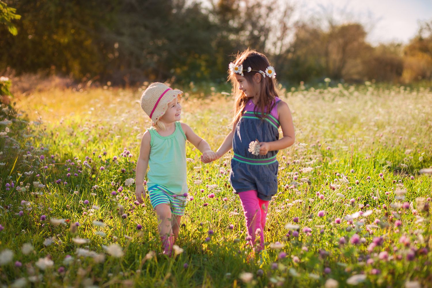 Children explore a wildflower meadow at sunset during golden hour, walking through tall grass and blooming flowers.