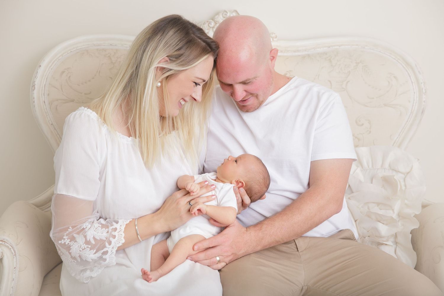 Tender moment between parents and newborn baby on cream colored couch.
