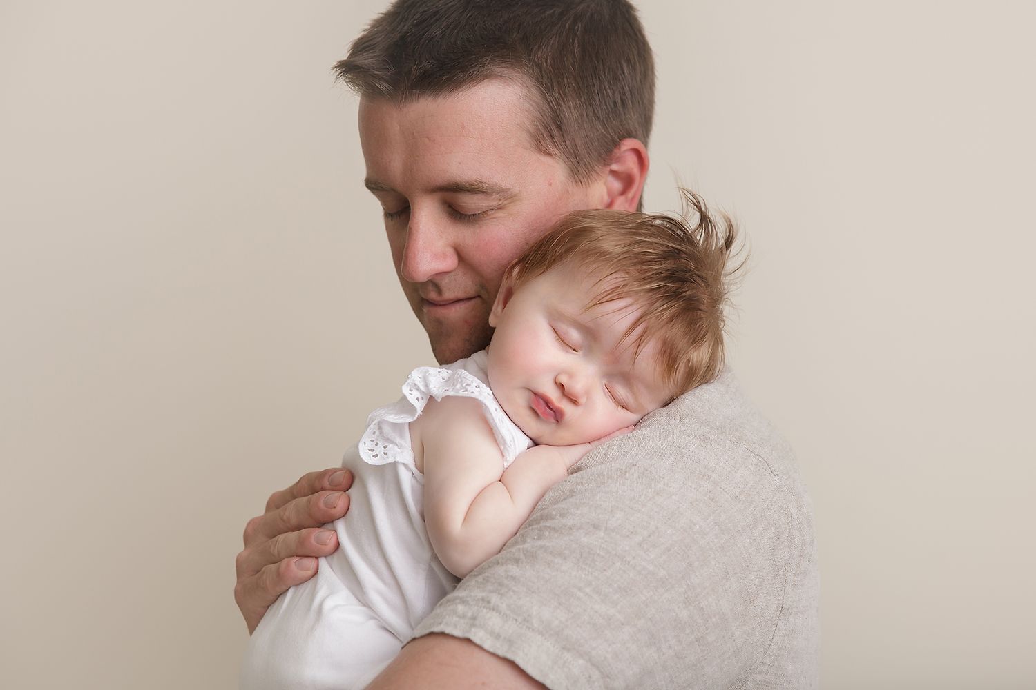 Tender moment between parent and sleeping child in white clothing.