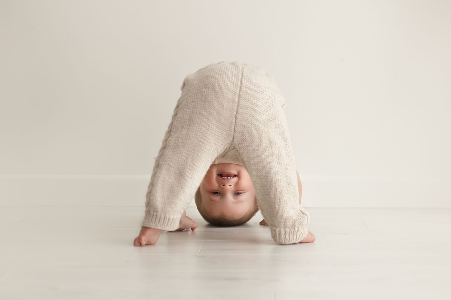 Baby crawling on white background wearing neutral colored outfit.