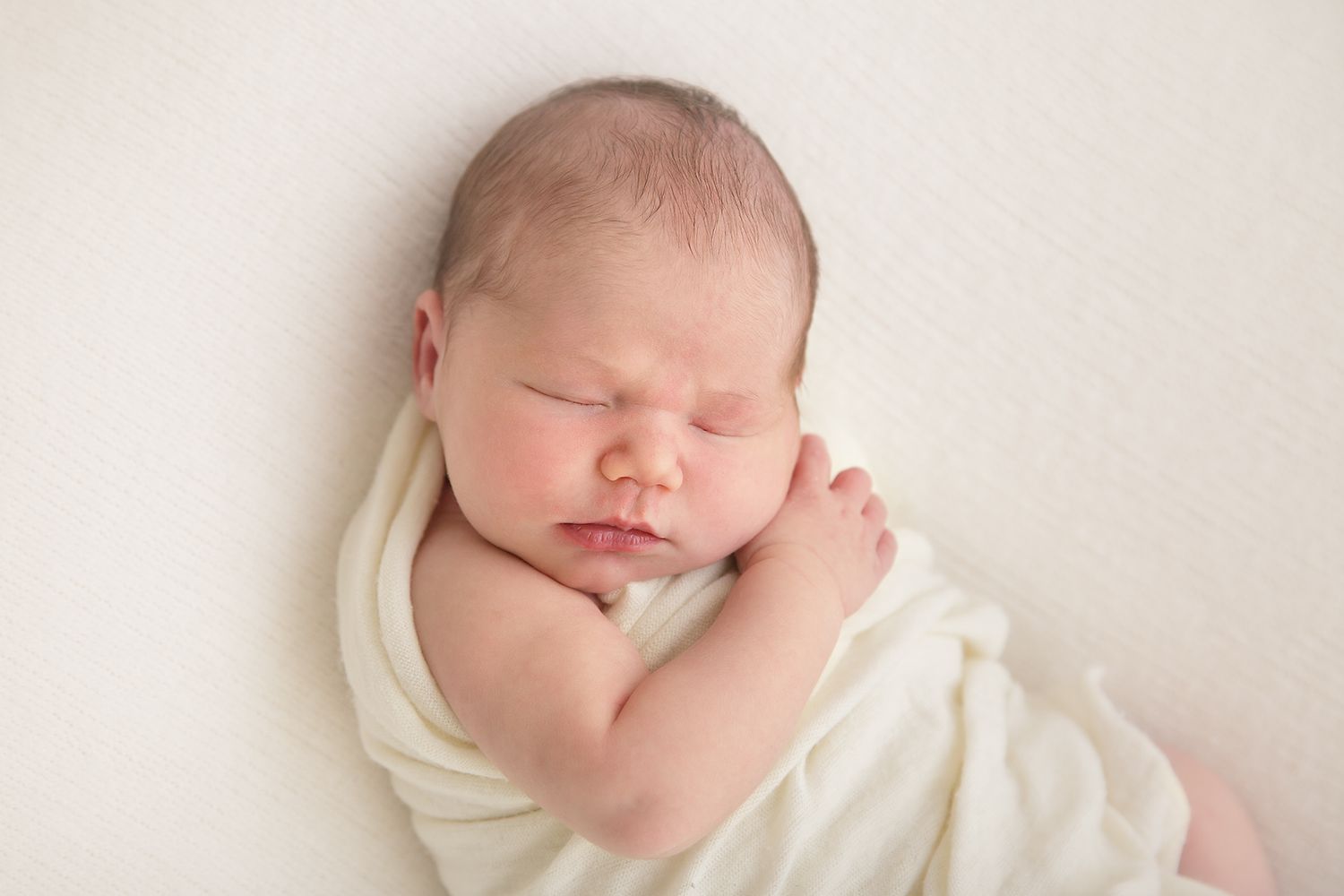 Newborn baby sleeping peacefully wrapped in soft ivory fabric.