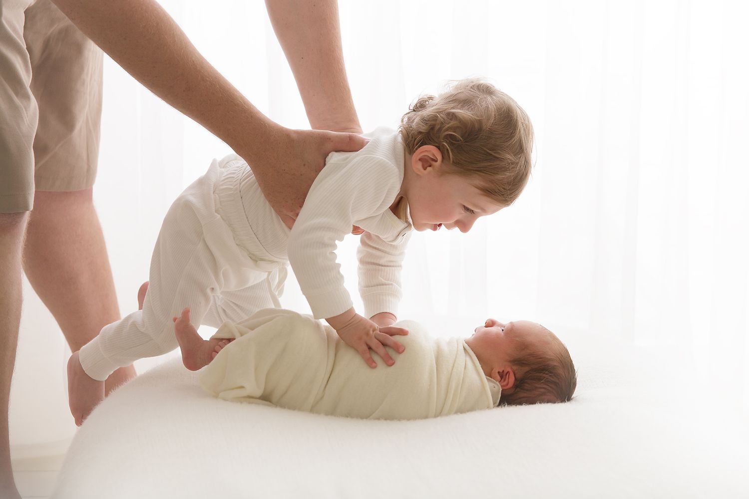 Parent and baby sharing playful interaction on white surface in bright room.