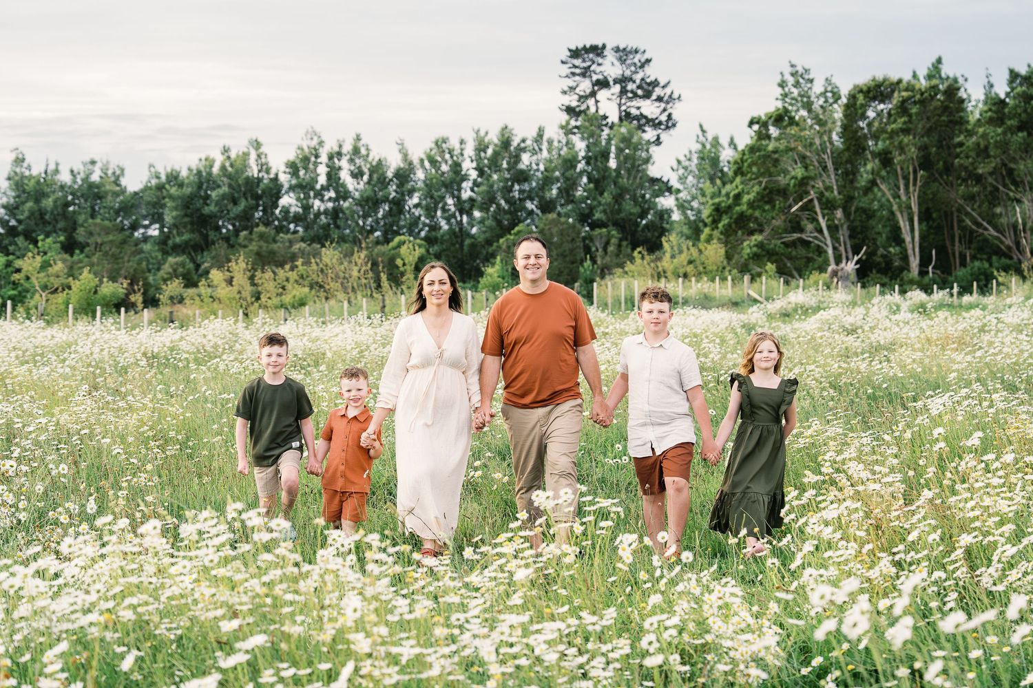 A group of people walking through a beautiful field of white wildflowers on a sunny summer day.