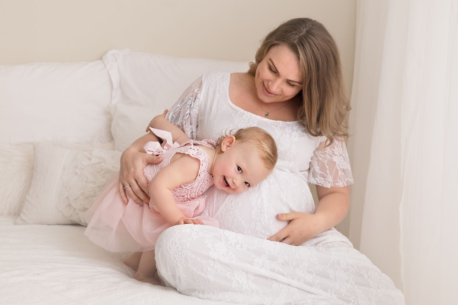 A tender family portrait session in soft white and pink tones against a neutral background.