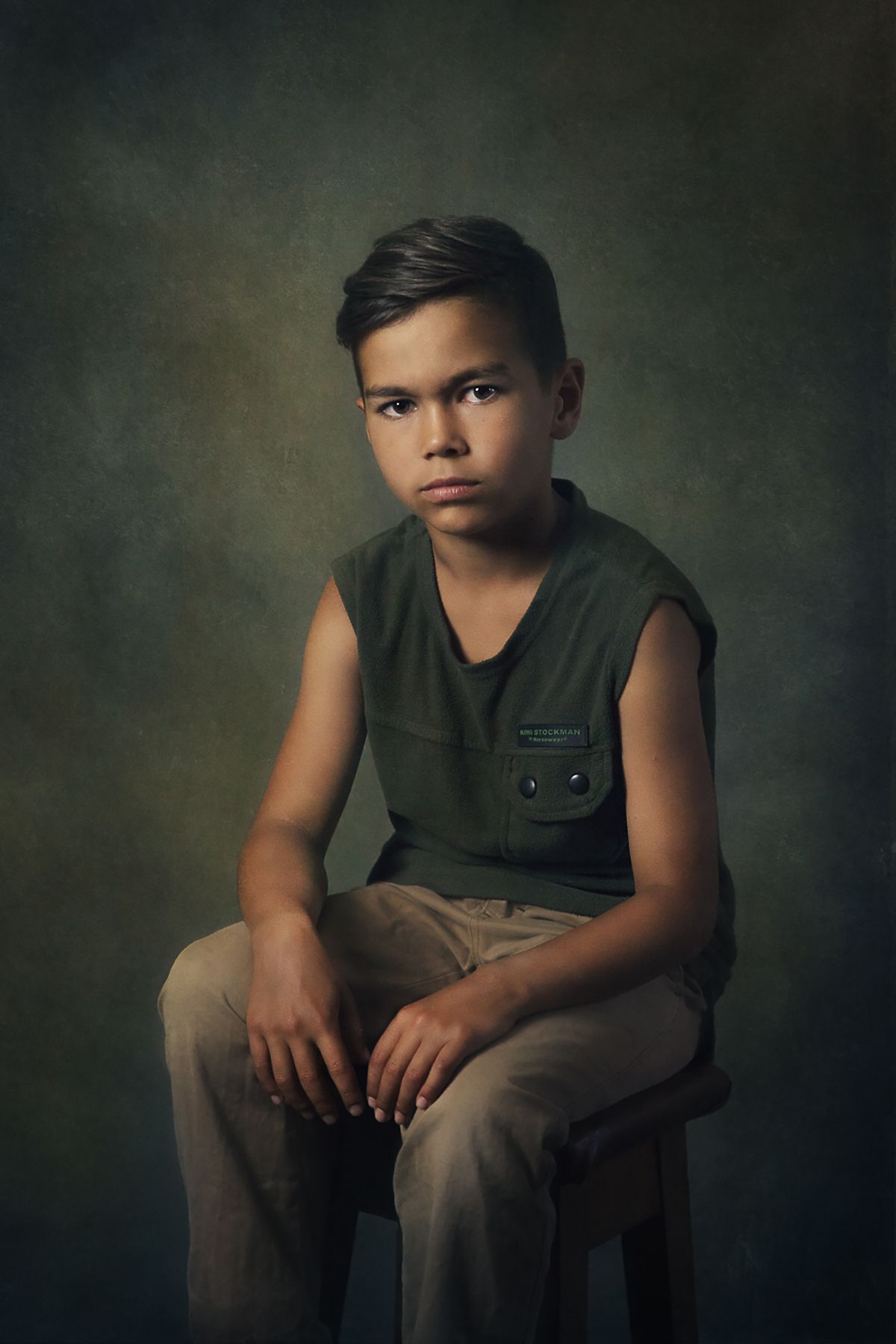 Moody portrait of a figure in olive green clothing against a textured dark background.