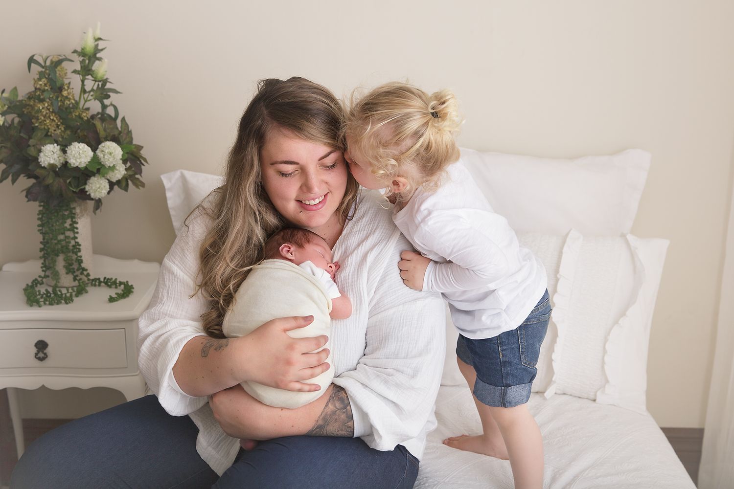 Family cuddle session on white bed with natural window light.