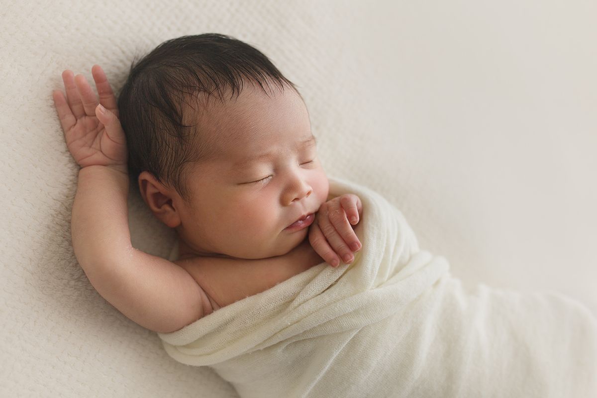 Sleeping newborn wrapped in soft cream fabric during studio portrait session.