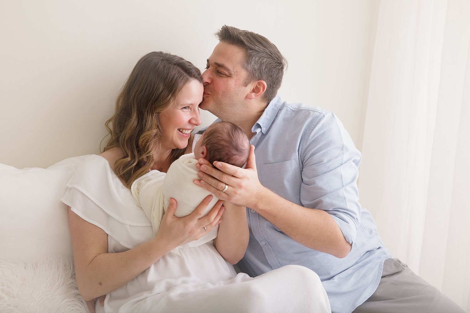 Tender moment between parents cuddling with their newborn baby in a bright white room.