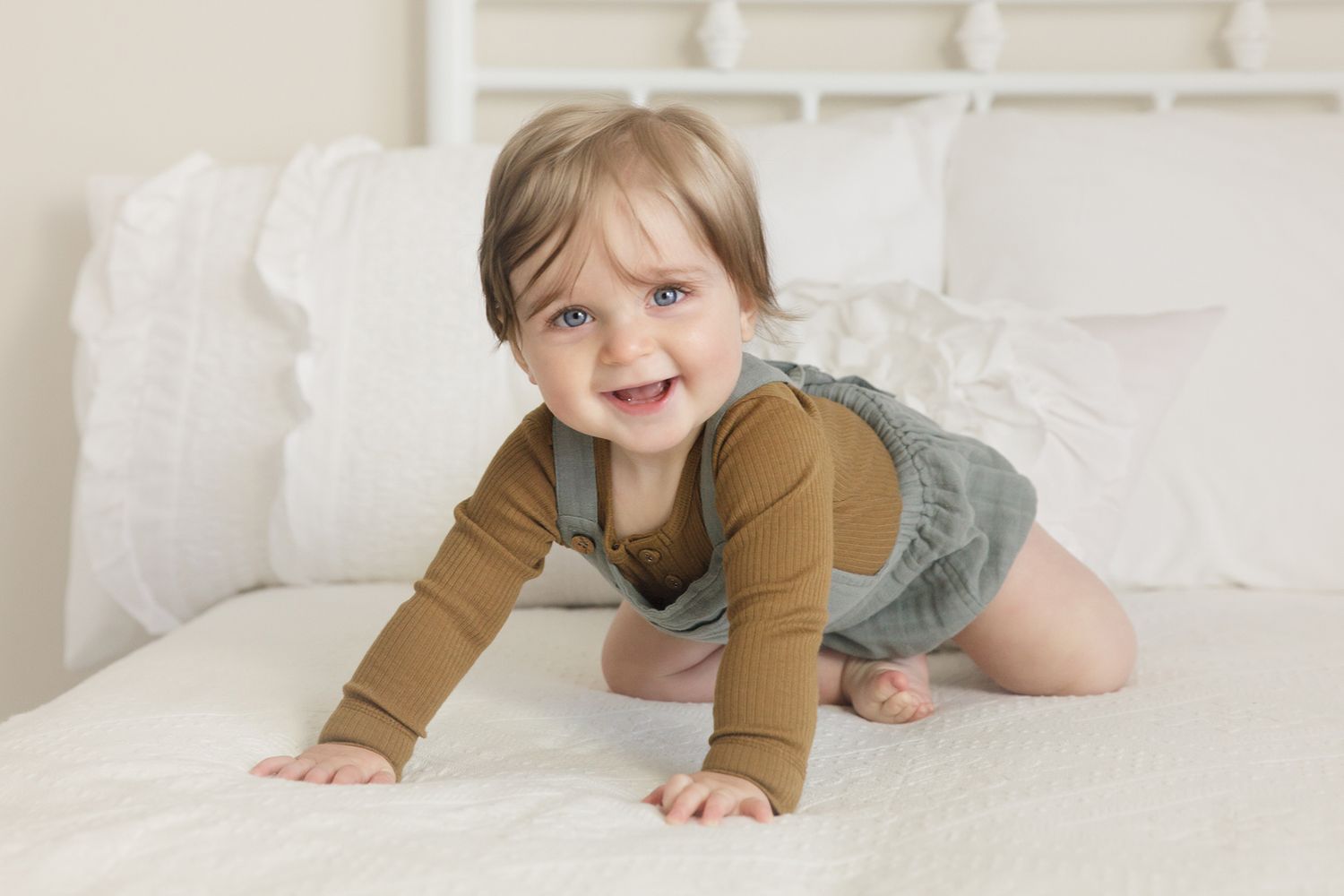 Baby in brown top crawling on white surface during photo session.