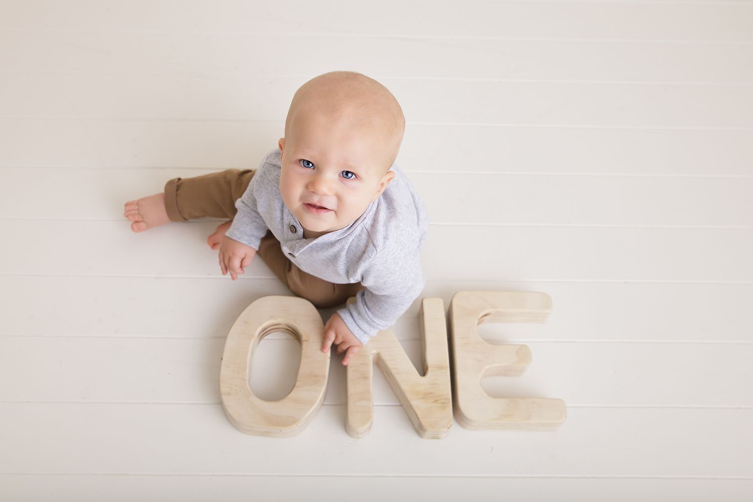 Baby photographed with wooden ONE letters during first birthday milestone session.