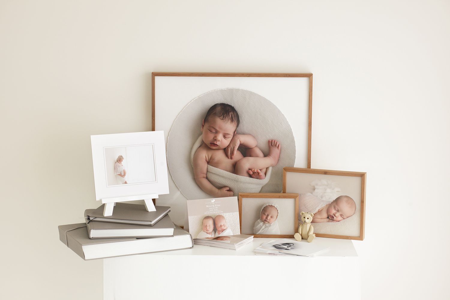 Collection of framed newborn photos displayed on white shelf with books.