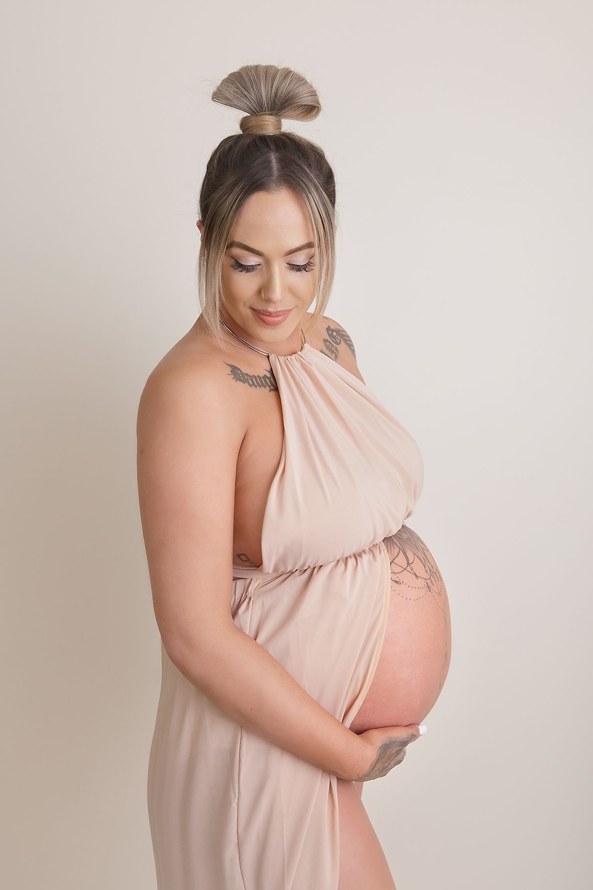Elegant maternity photos featuring a blush pink halter dress against a neutral backdrop.