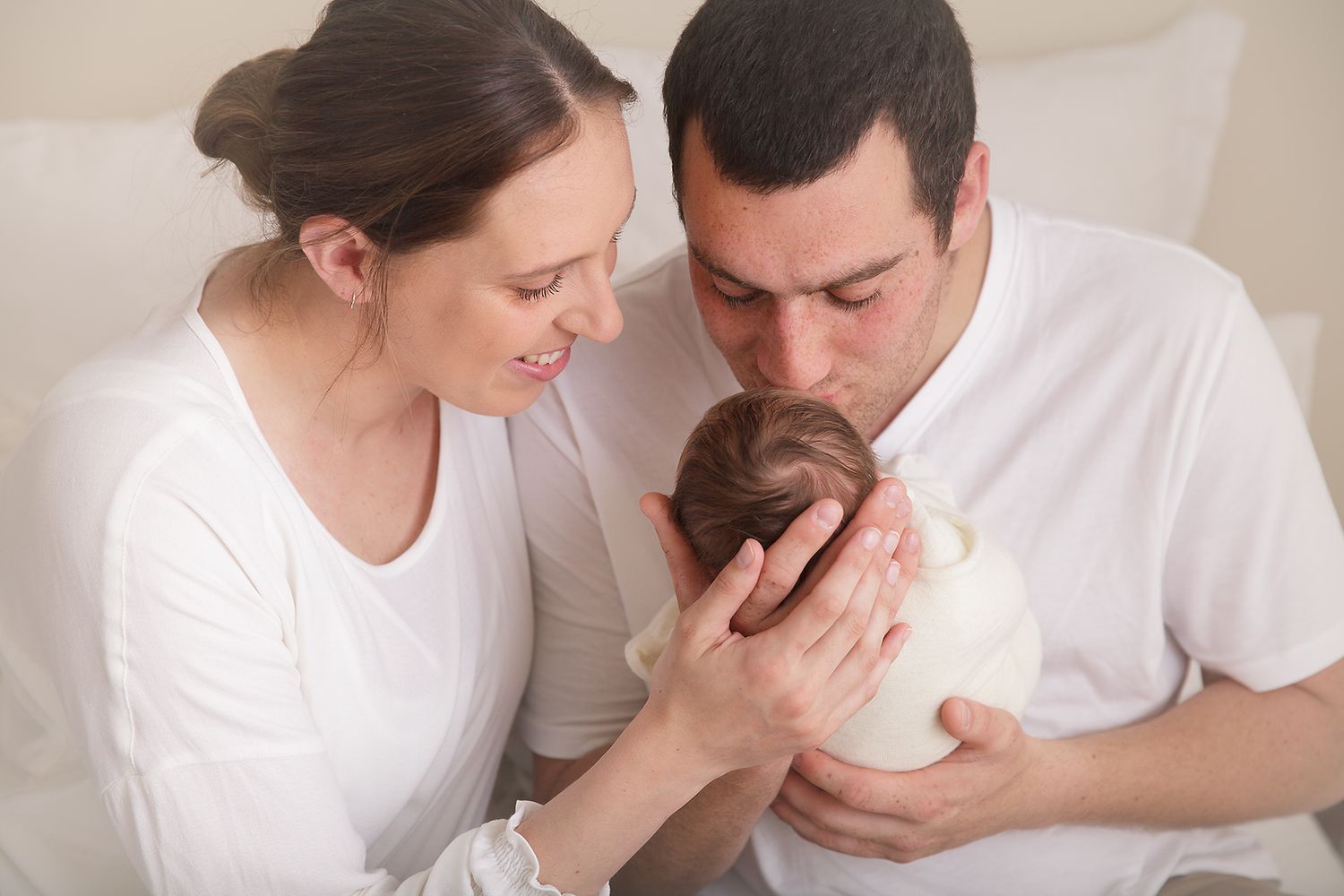 Parents sharing an intimate moment with their newborn baby against white background.