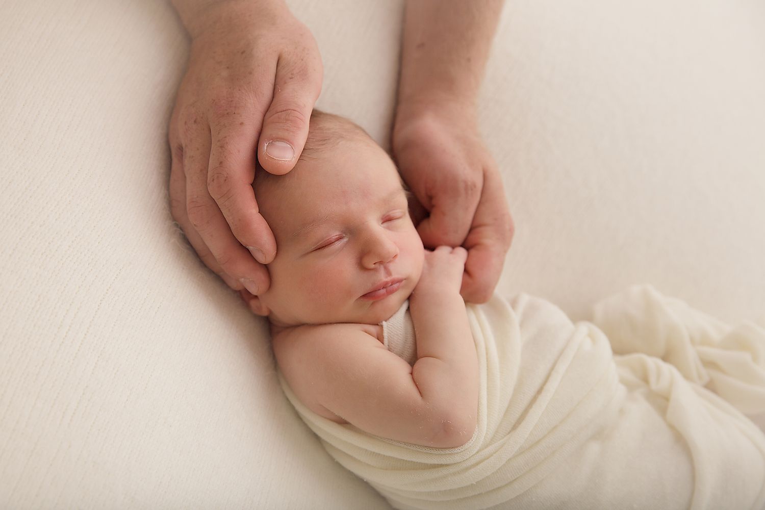 Sleeping newborn baby wrapped in soft white fabric during professional photo session.