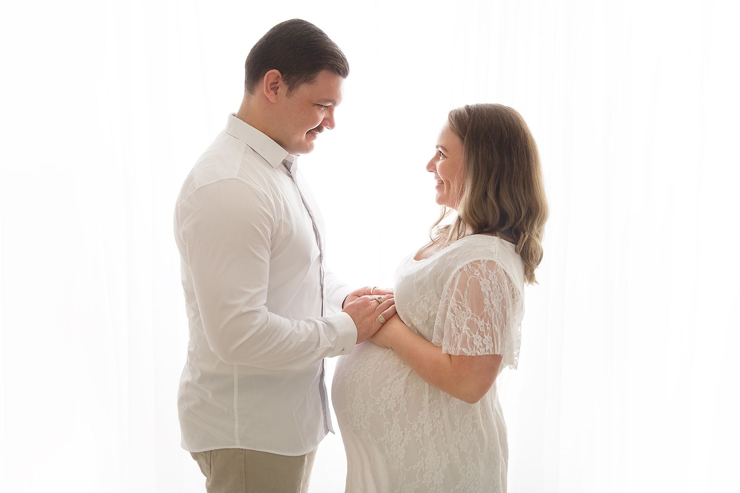 Bright white studio maternity session capturing tender moments between expectant couple.