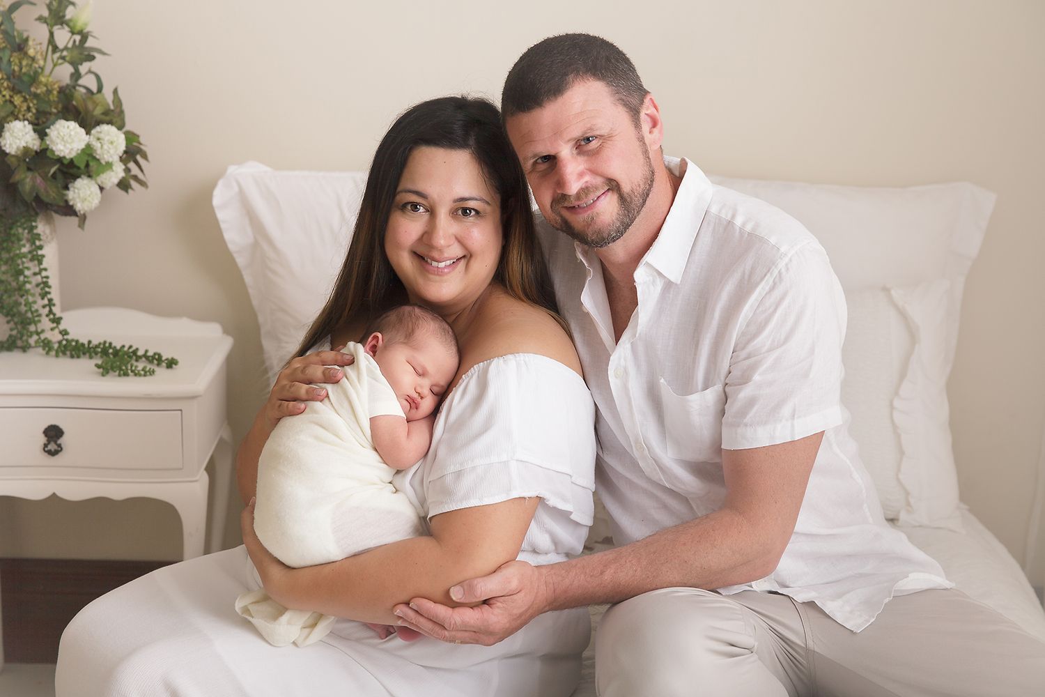 Family portrait with newborn baby on white bed with floral decorations.