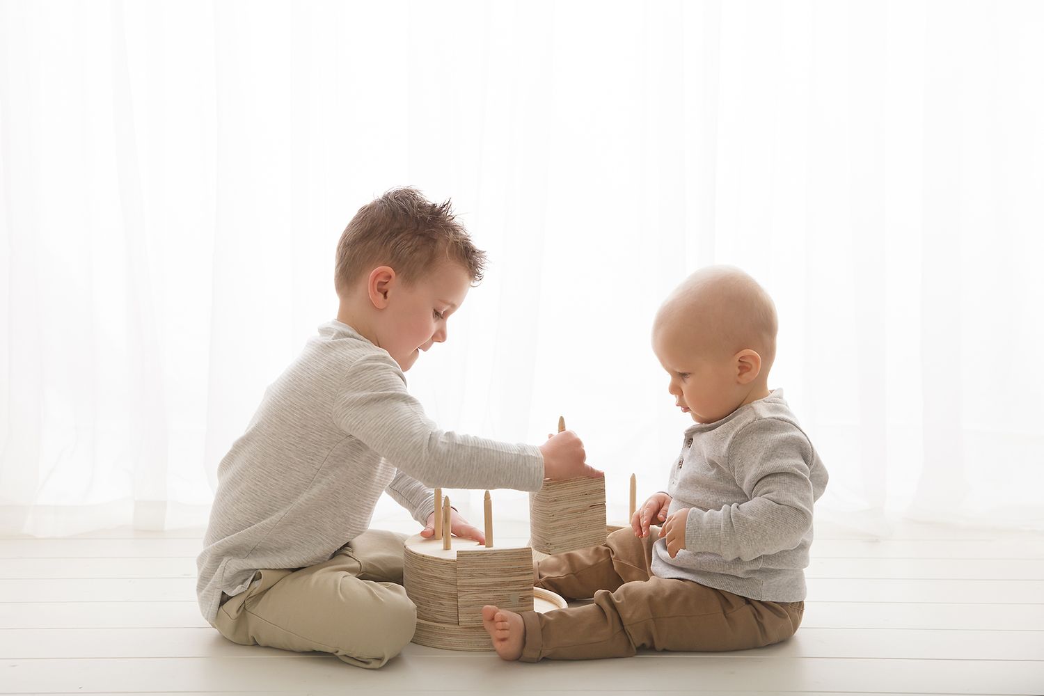Two babies playing with wooden blocks on white floor.