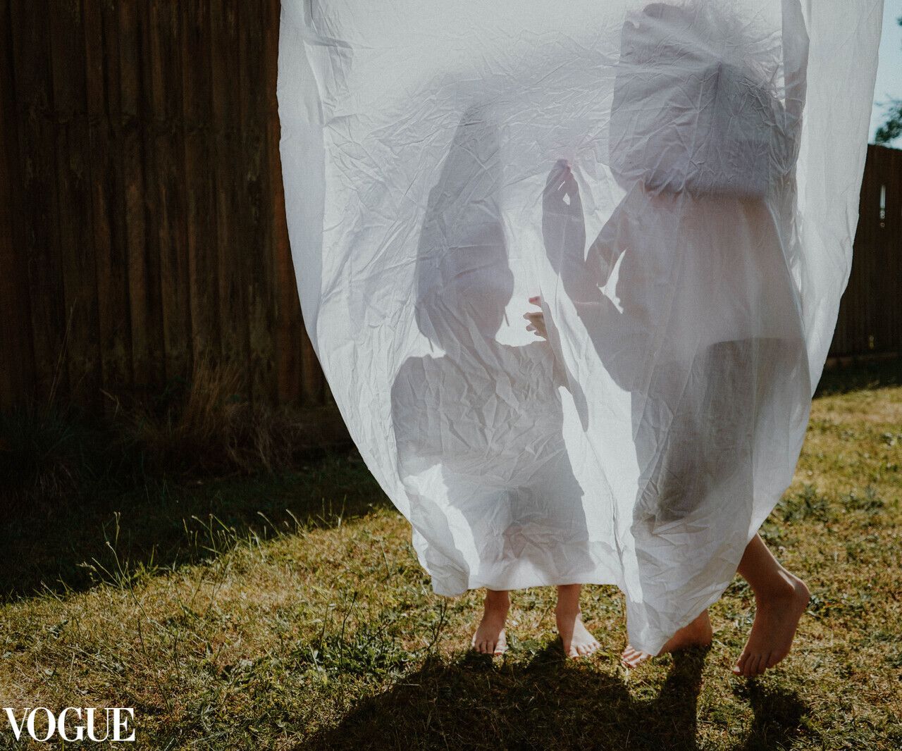 Silhouettes behind white fabric sheet hanging on clothesline on sunny day.