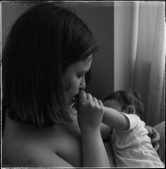 A tender black and white portrait showing a person holding and caring for a baby near a window.