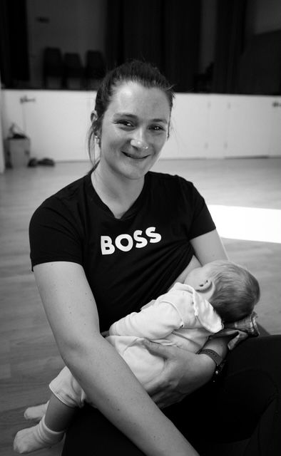Black and white photo of person wearing a BOSS t-shirt holding sleeping infant in indoor setting.