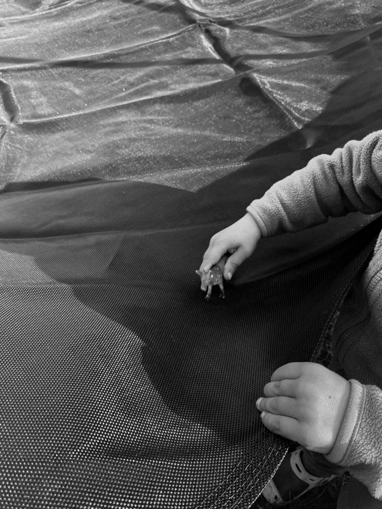 Hands reaching across a textured mesh surface in grayscale.