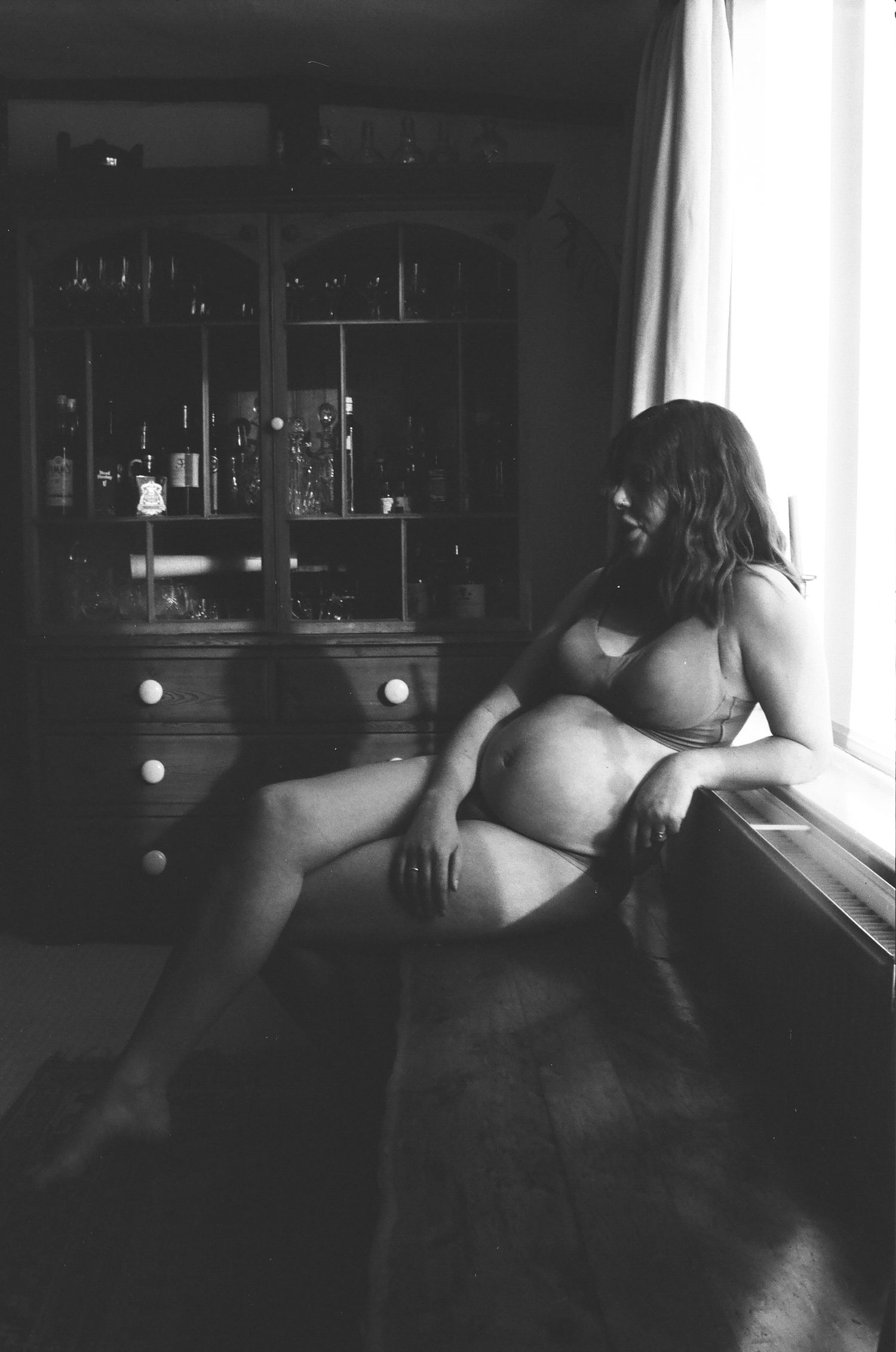 Black and white boudoir maternity photo featuring an intimate window portrait in natural light.