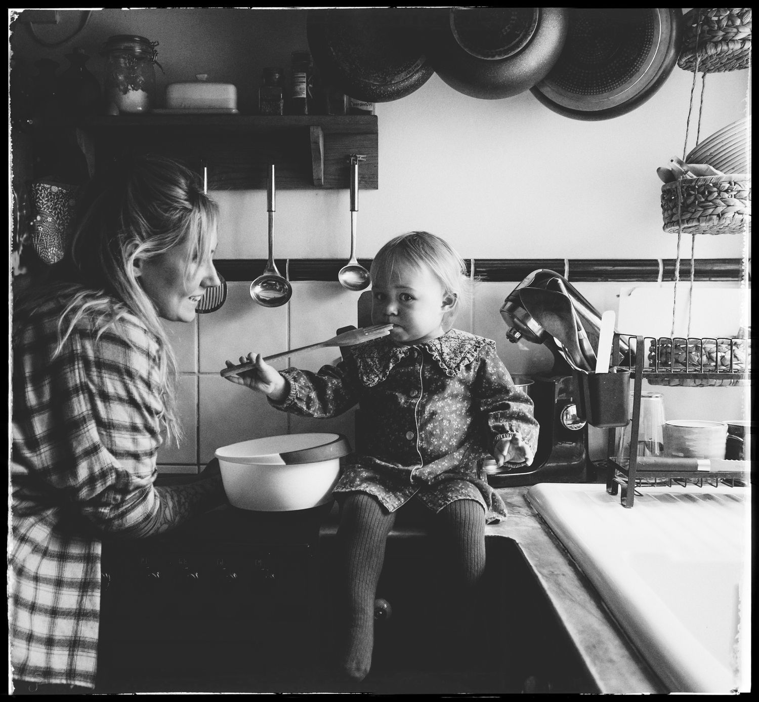 Vintage black and white kitchen scene showing companionship and conversation over a mixing bowl during baking.