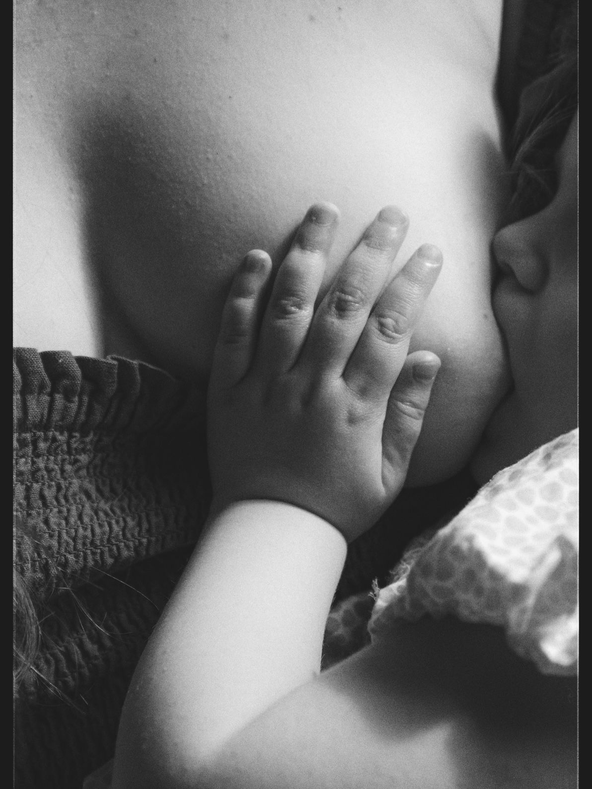 A black and white artistic photograph shows a hand covering part of a bare torso in dramatic lighting.