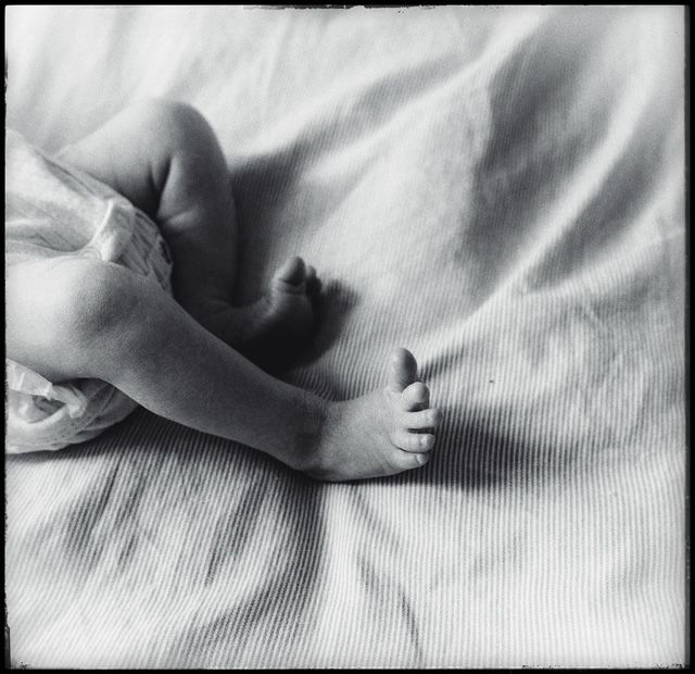 Artistic black and white close-up photograph of small infant hands resting on white fabric.