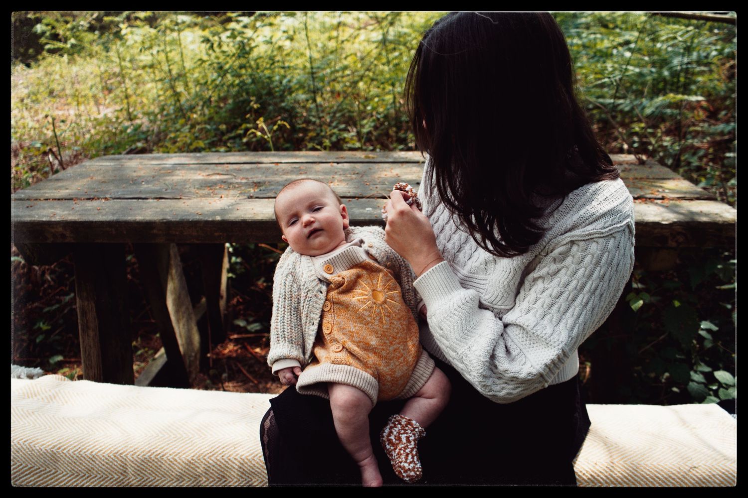 A parent and small child sitting together on a stone bench in an outdoor garden setting.