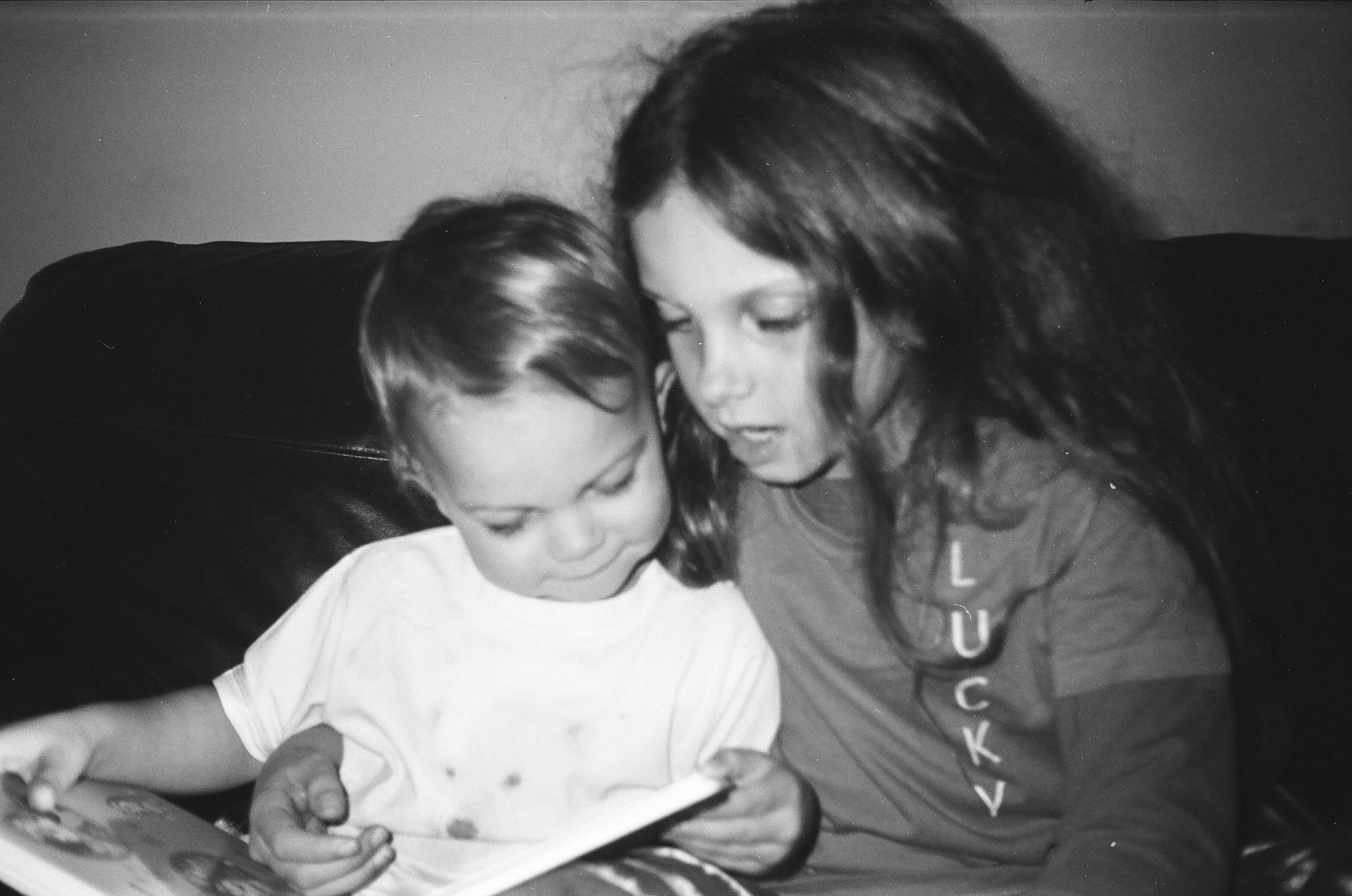 Vintage black and white photograph of two children reading together on a couch.