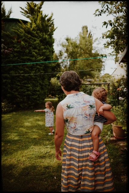 People wearing matching striped dresses stand in a lush garden setting on a sunny afternoon with trees in background.