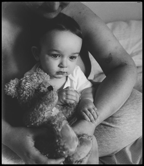 A vintage black and white photograph of a small child holding a teddy bear while sitting next to someone.