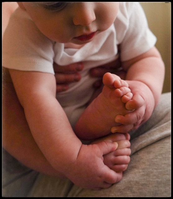 Baby's tiny fingers holding each other against a soft gray fabric background.