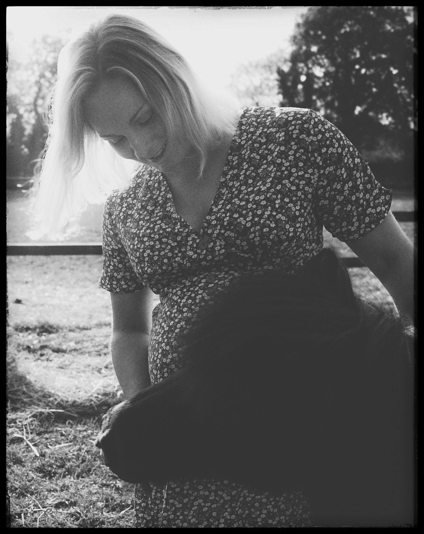Person in patterned dress sitting outdoors on grass in black and white photography.